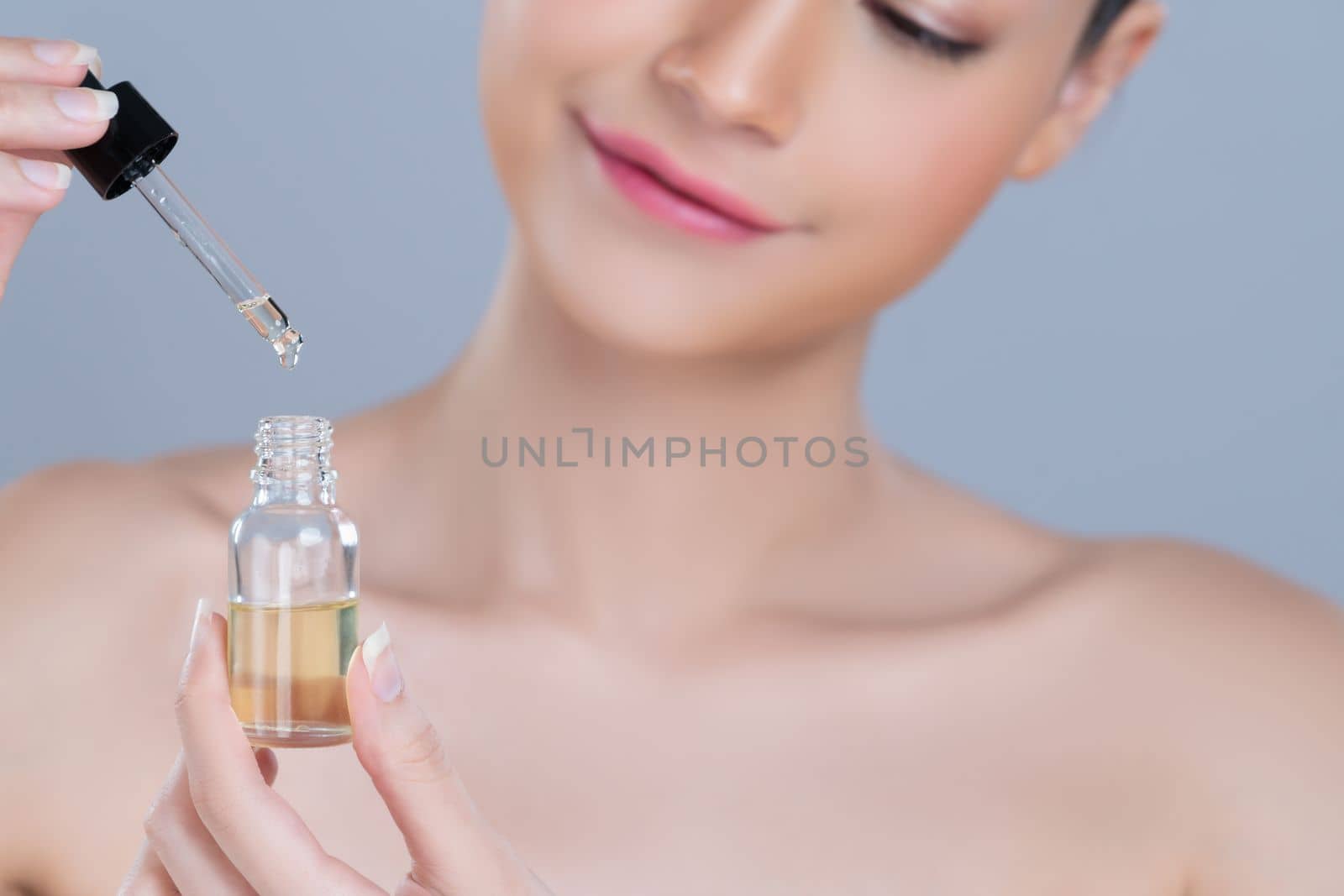 Focus cannabis extracted oil bottle with dropper lid holding by blurred glamorous beautiful asian woman with perfect clean skin and soft smooth makeup in isolated background.