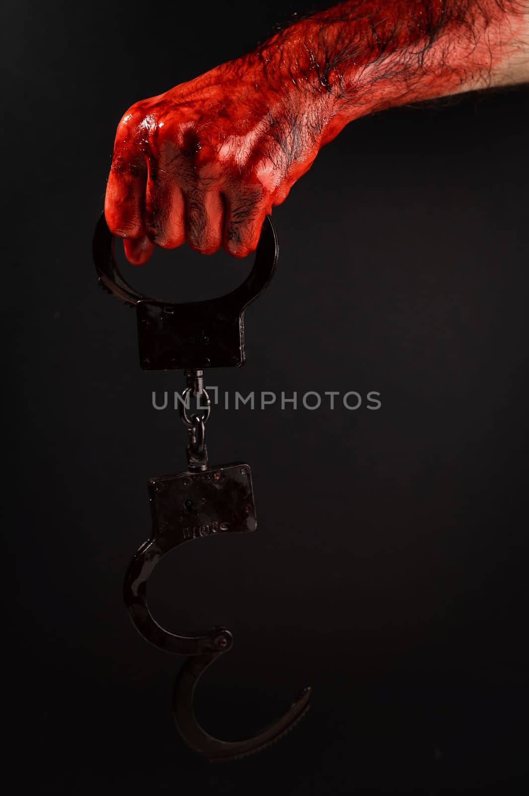 Faceless man holding handcuffs black background. Hands are stained with blood