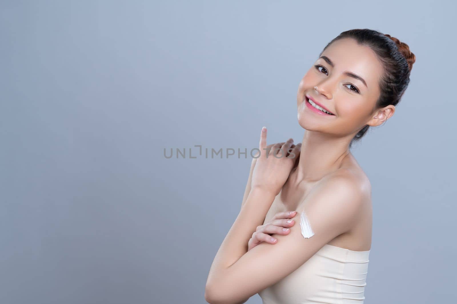 Glamorous beautiful woman applying moisturizer cream on her arm for perfect skincare treatment in isolated background. Soft makeup young girl portrait with skin rejuvenation and cosmetology concept.
