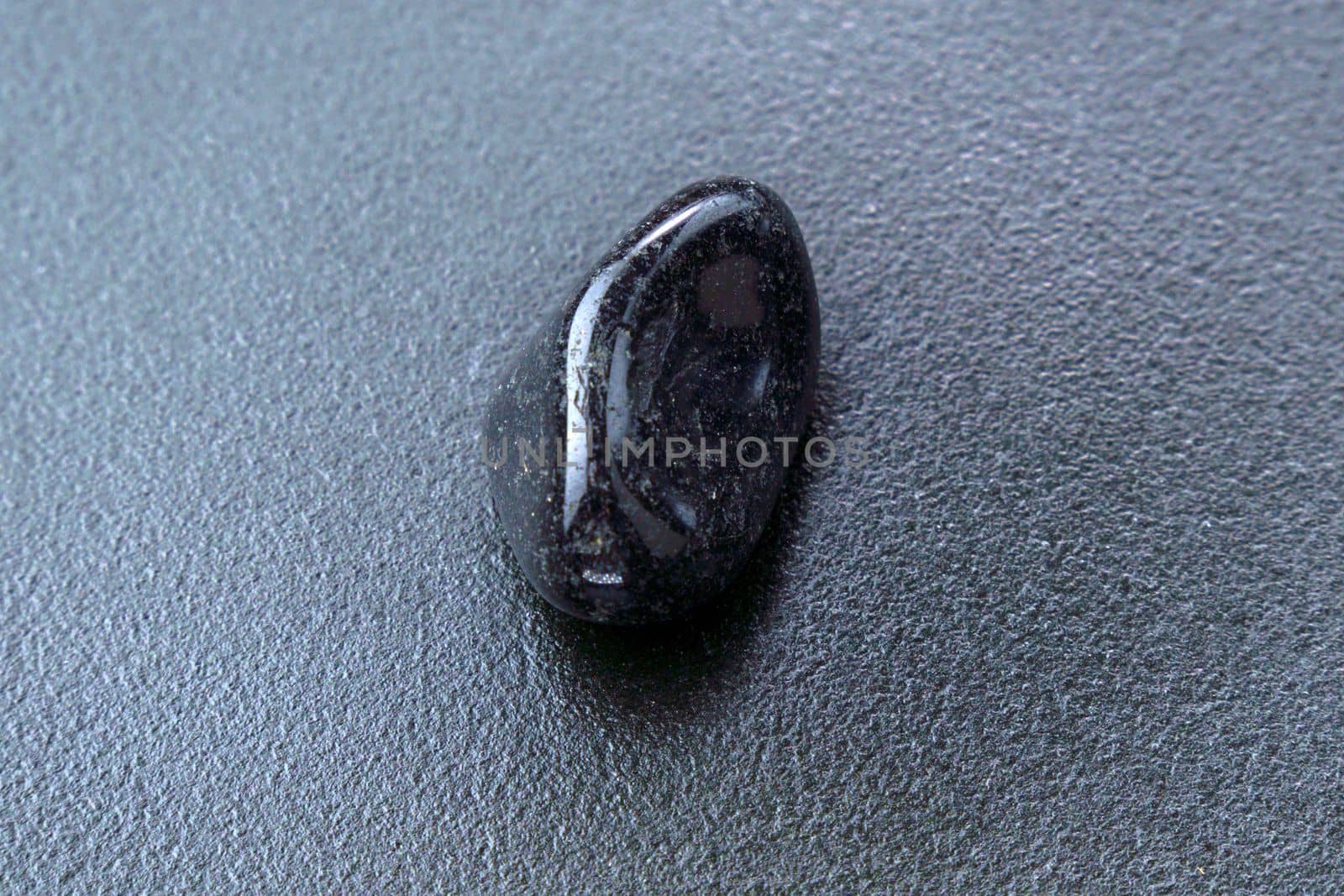 Close up of natural mineral from geological collection tumbled black onyx gem stone, black background