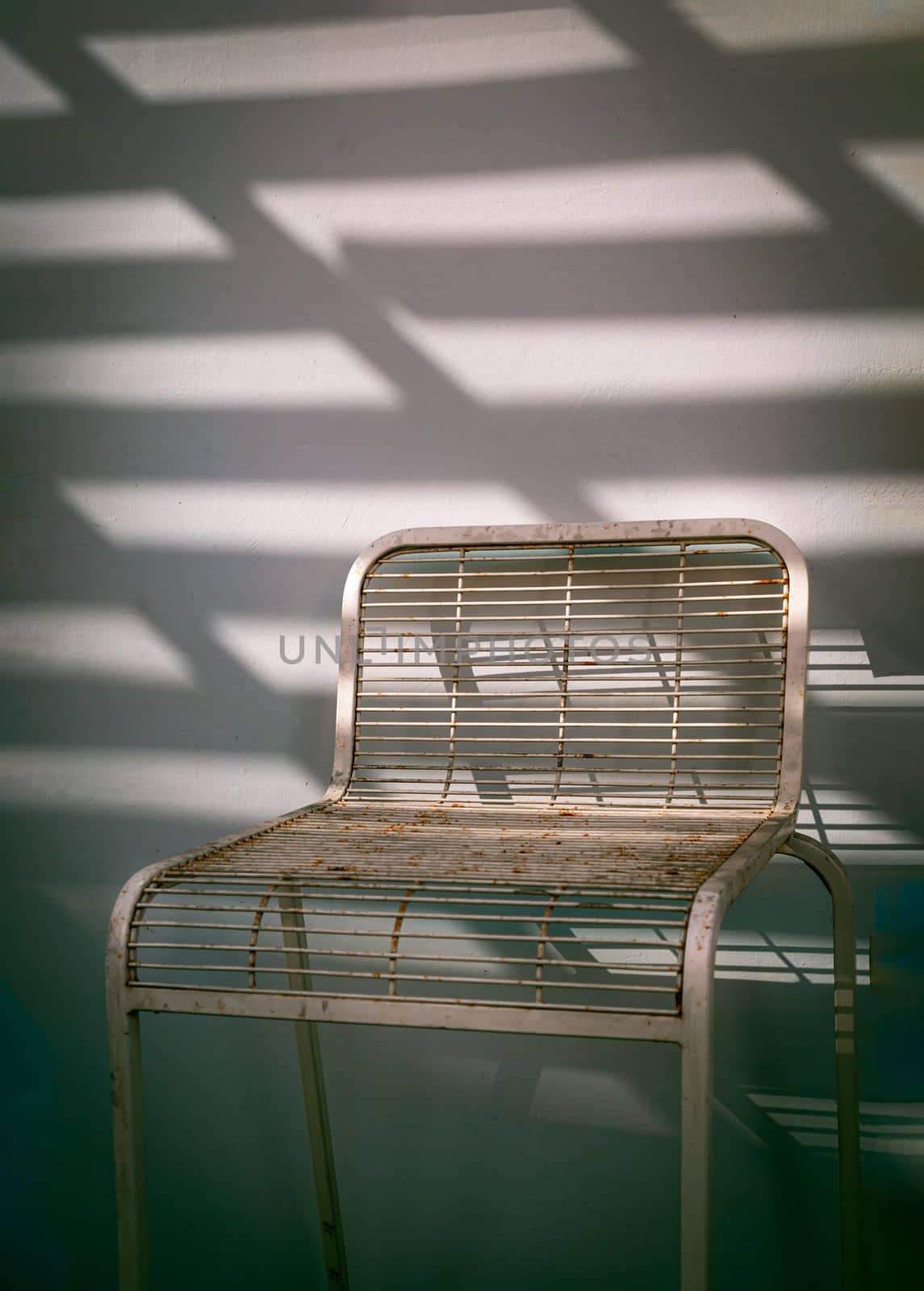 The metal chair is stand alone in front of the white wall with Sunbeam shine through in the morning. Retro style, Copy space, Selective focus.