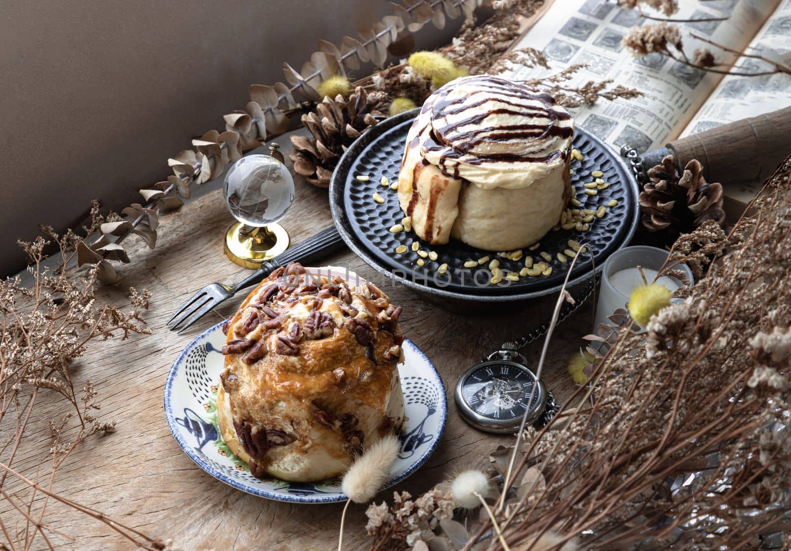 Two Homemade Soft Chocolate Buns, Caramel Pecanbon topped with caramel frosting and pecans and Cinnamon roll topped with rich cream cheese frosting served with Metal fork on old rustic wooden table. The concept of delicious dessert, Top view, Selective focus.