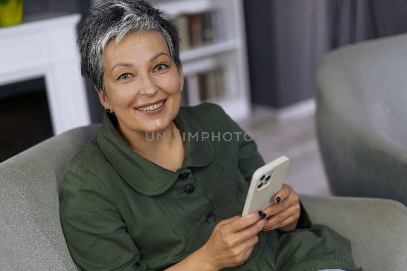 Happy woman is smiles brightly indoors. Surrounded by the warmth of her home, she exudes sense of contentment and peace. Her smile is contagious, spreading positivity. High quality photo.