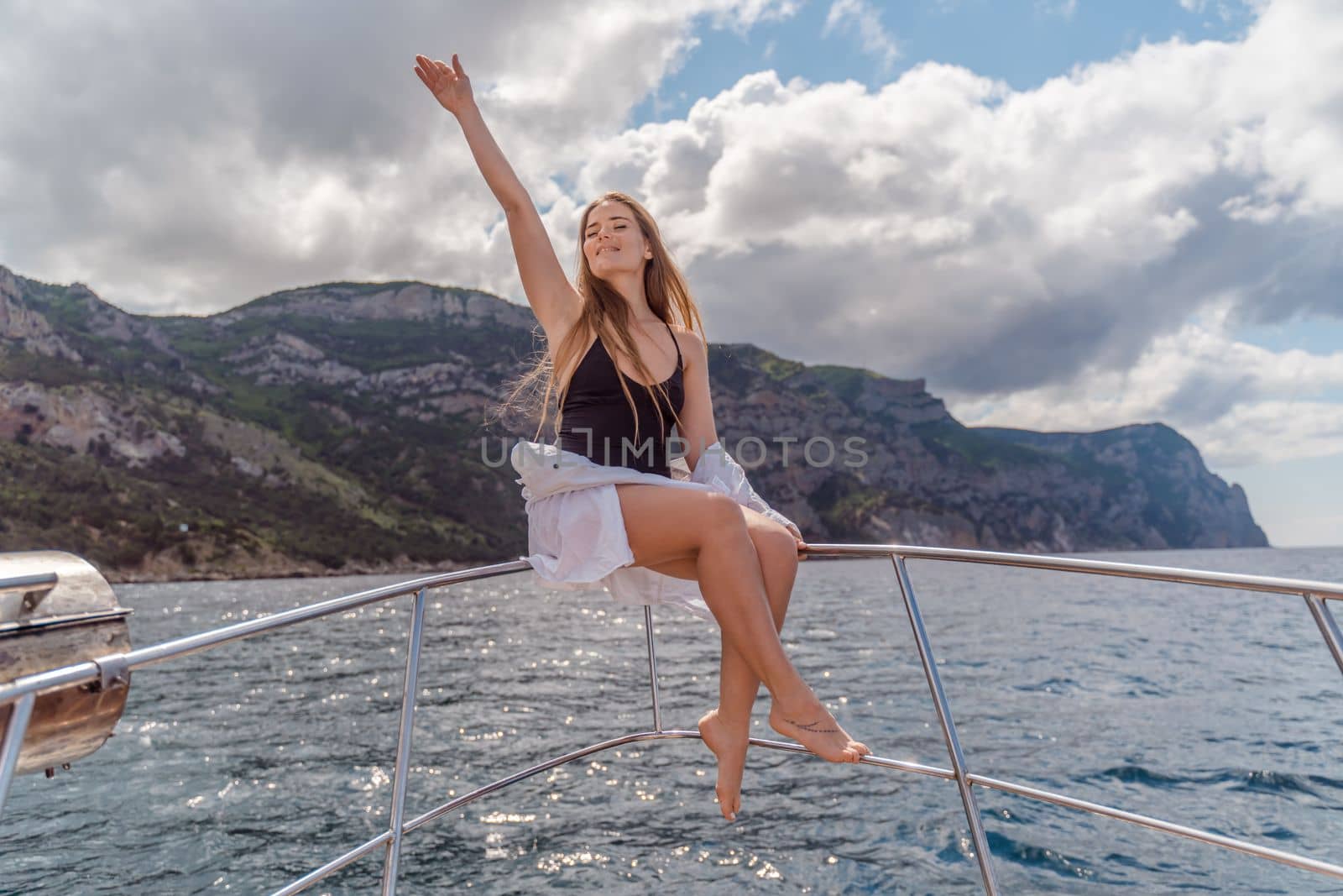 Woman on a yacht. Happy model in a swimsuit posing on a yacht against a blue sky with clouds and mountains.