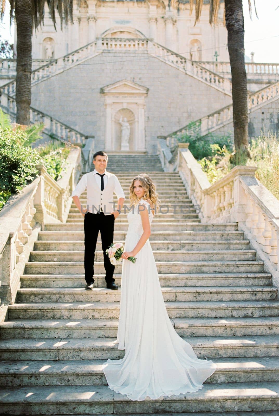 Bride and groom stand on the stone steps of the Church of the Nativity of the Virgin in Prcanj. Montenegro. High quality photo
