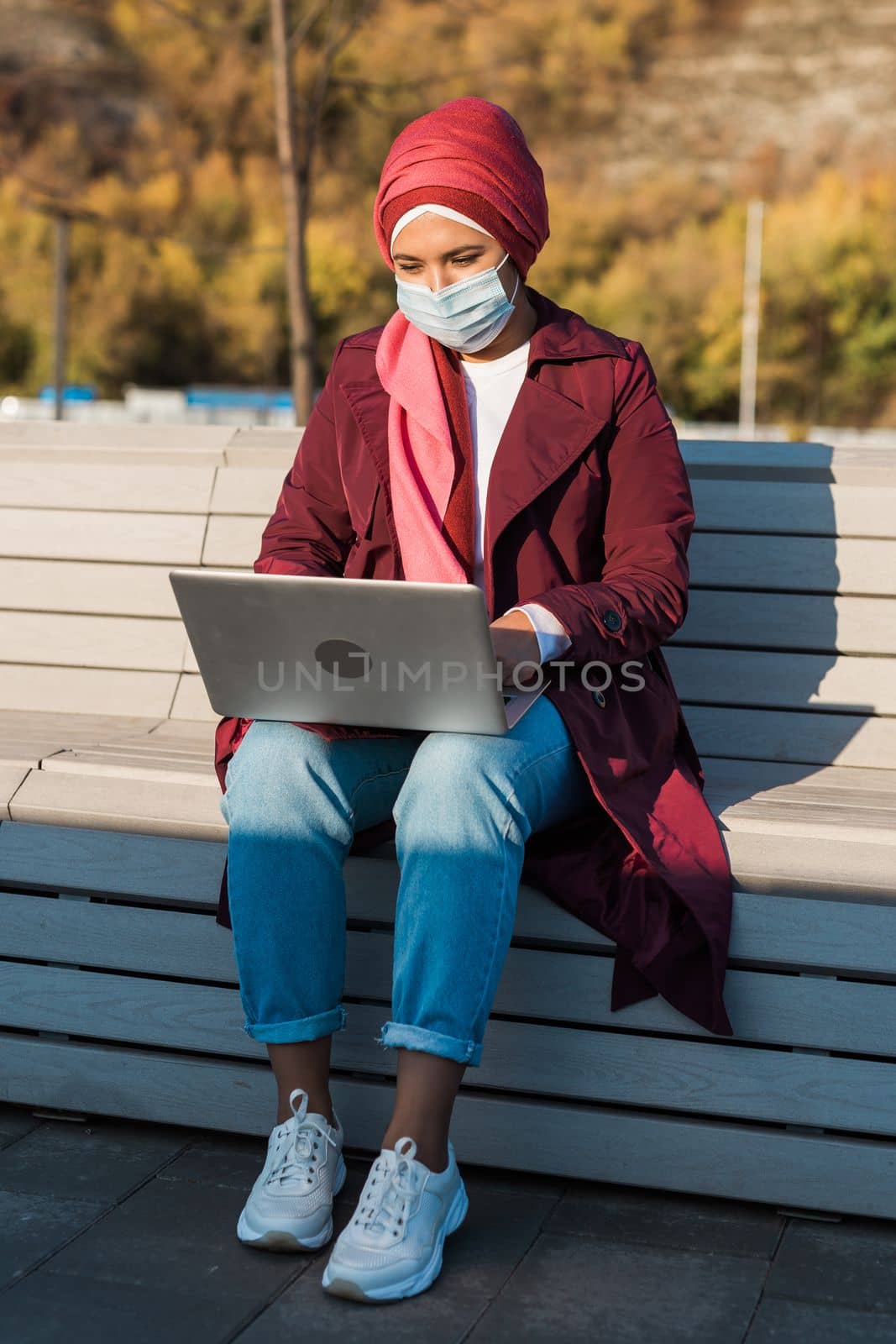Muslim arab woman wears hijab and blue protective medical mask works online on laptop and video communication via Internet - social networks, business and video call concept by Satura86