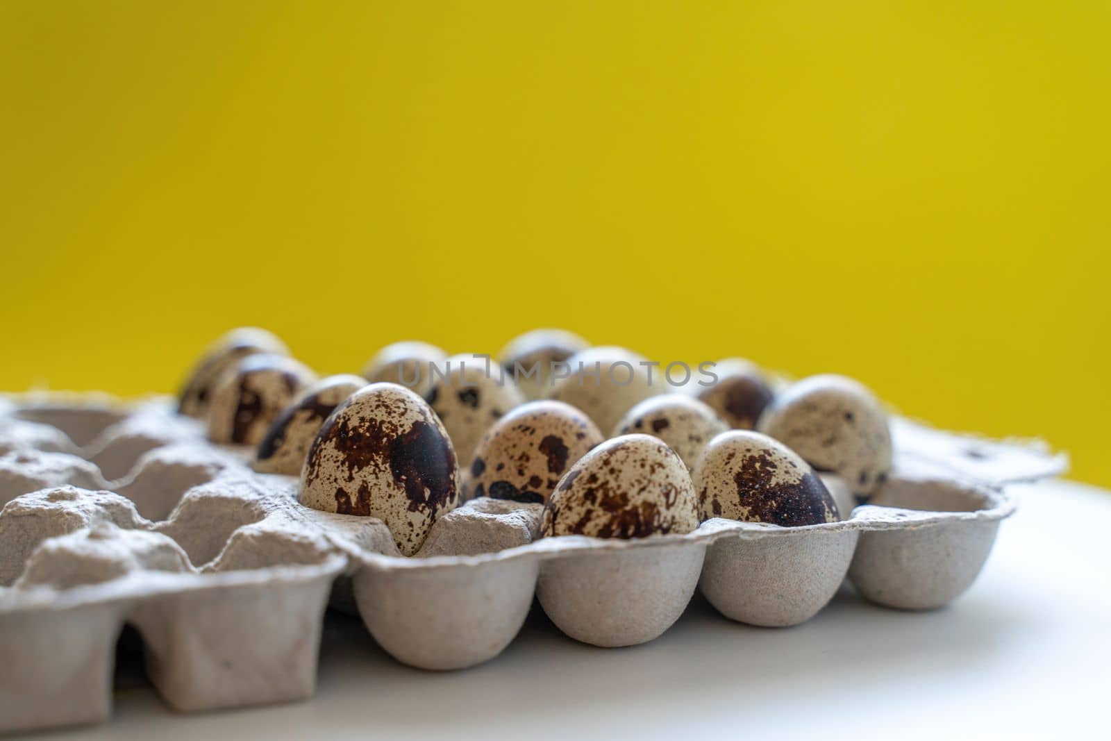 Spotted quail eggs in an egg box on a yellow background, natural eco friendly products. by Matiunina