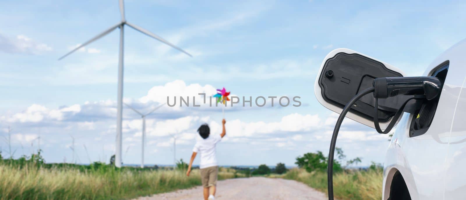 Progressive young asian boy playing with wind pinwheel toy in the wind turbine farm, green field over the hill. Green energy from renewable electric wind generator. Windmill in the countryside concept