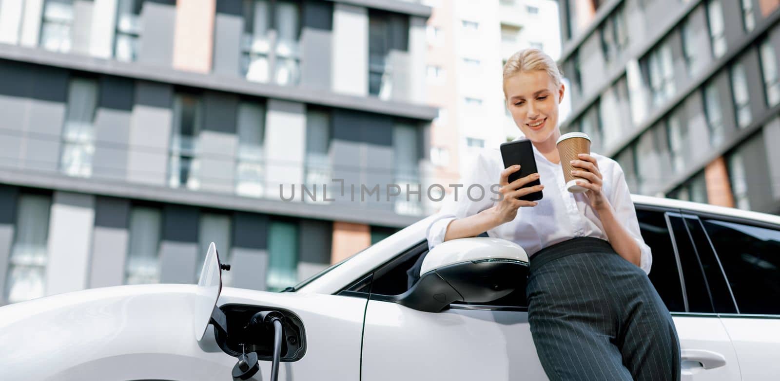 Focus progressive woman using phone and holding coffee at charging station. by biancoblue