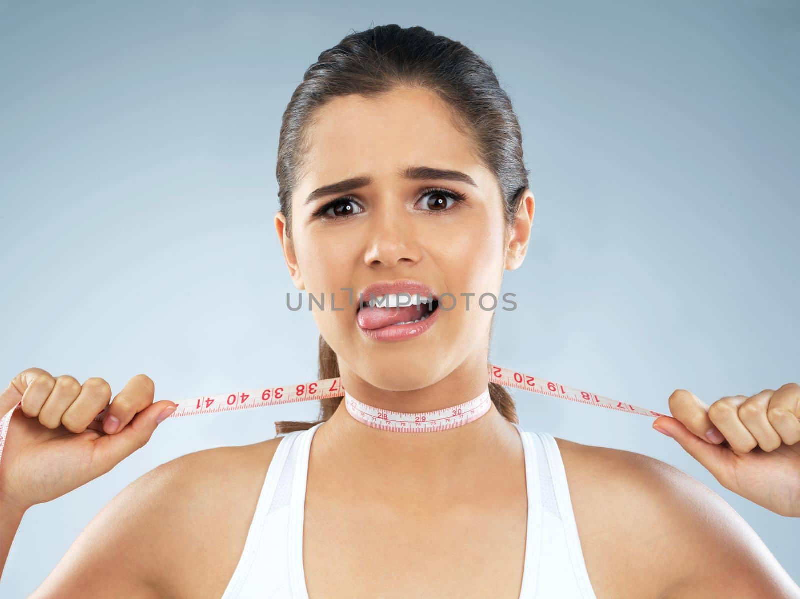 Dieting will be the death of me. Studio portrait of an attractive young woman with a measuring tape wrapped around her neck against a grey background