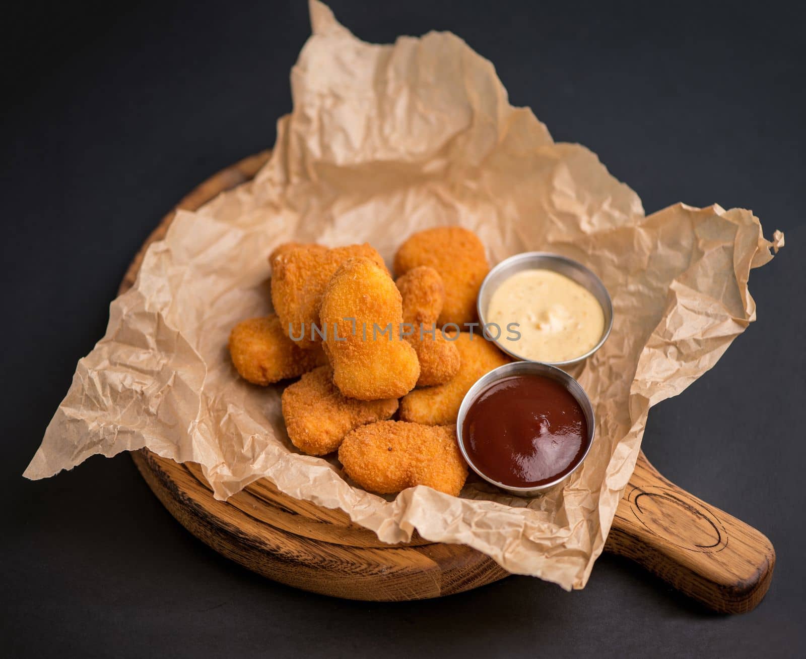 Side view of fried chicken fillet in panko breadcrumbs served with lettuce. sweet and sour sauce in saucepan near dish isolated on black background.