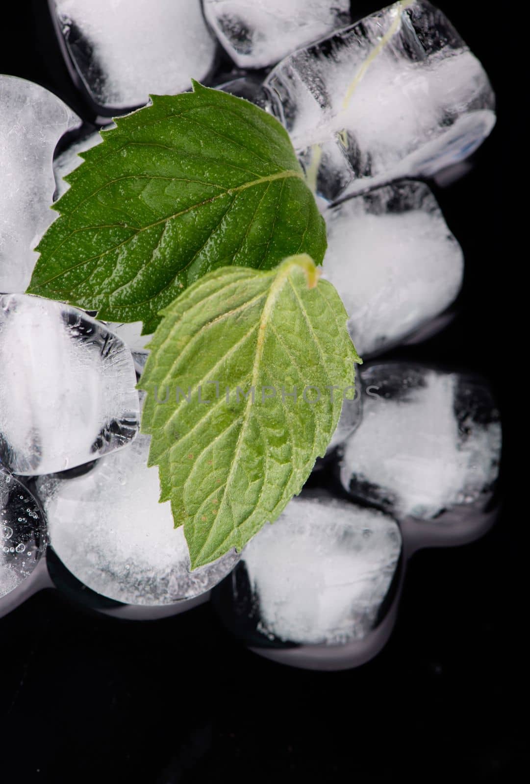 Ice cube with mint leaves on black background