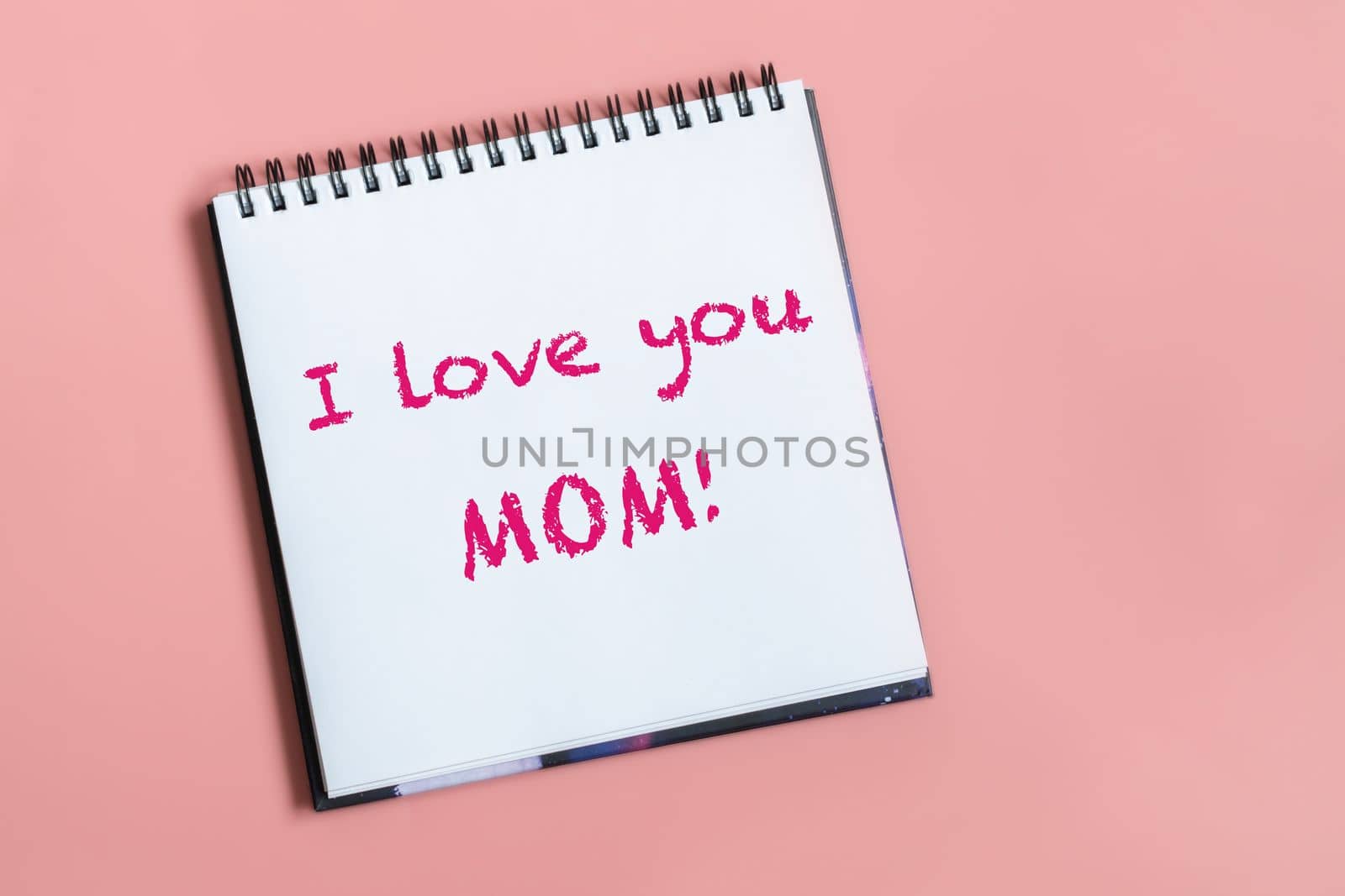 Text words I love you mom on sheet of paper. Happy mothers day concept. Pastel pink background.