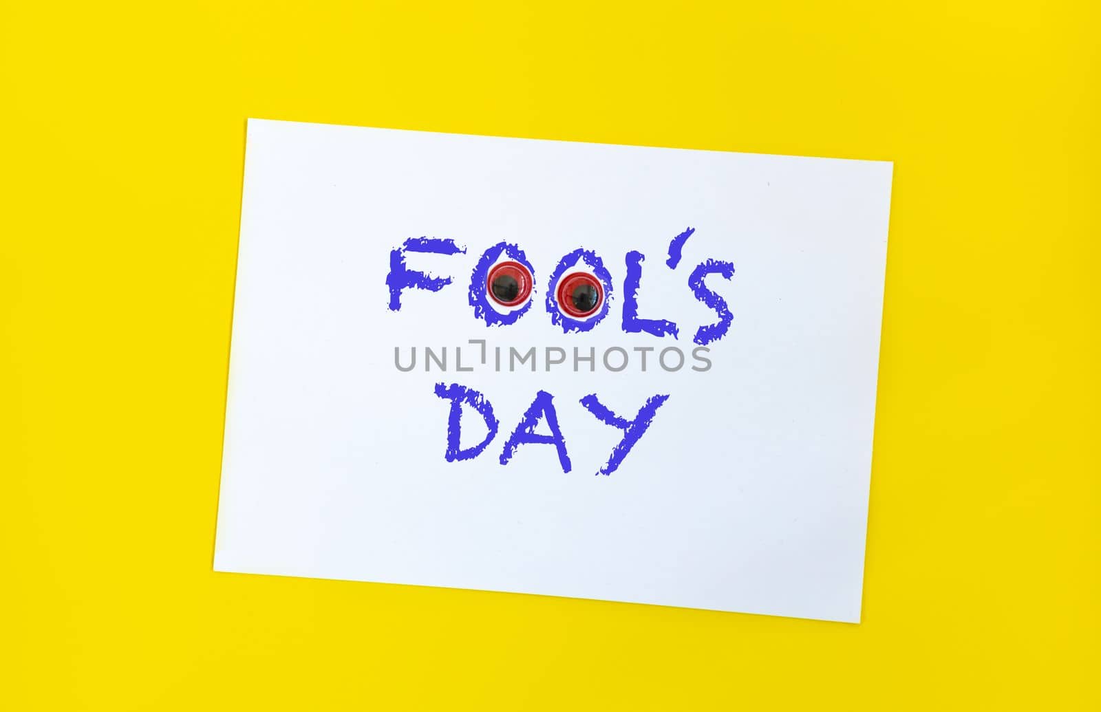 Text word Fool's day on sheet of paper with funny eyes and. 1 april message handwritting on sheet of paper. Bright yellow background. International humor day.