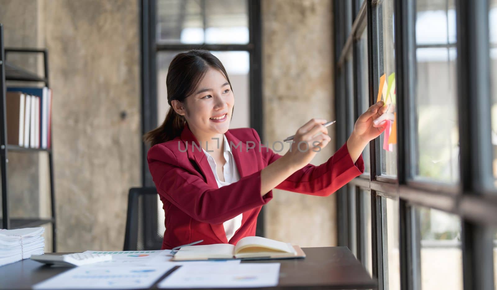 Young businesswoman creative team using post it notes in glass wall to writing strategy business plan to development grow to success...