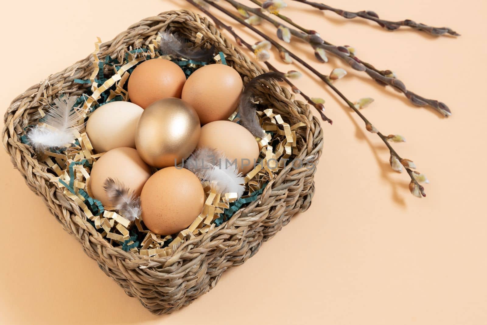 Easter eggs natural and gold in basket with feather. Branch of willow catkins. Light pastel orange background with copy space by Ri6ka