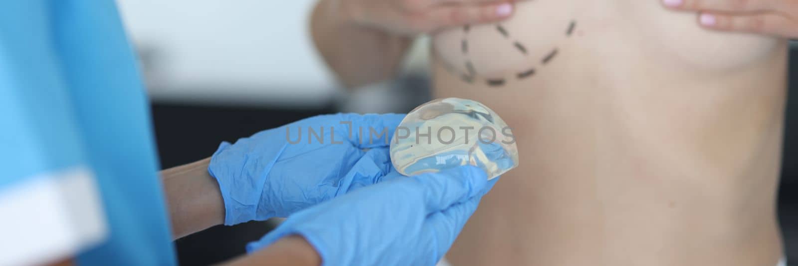 Doctor draws marks on female breast before cosmetic surgery operation and holds silicone implant. Breast augmentation and lift concept