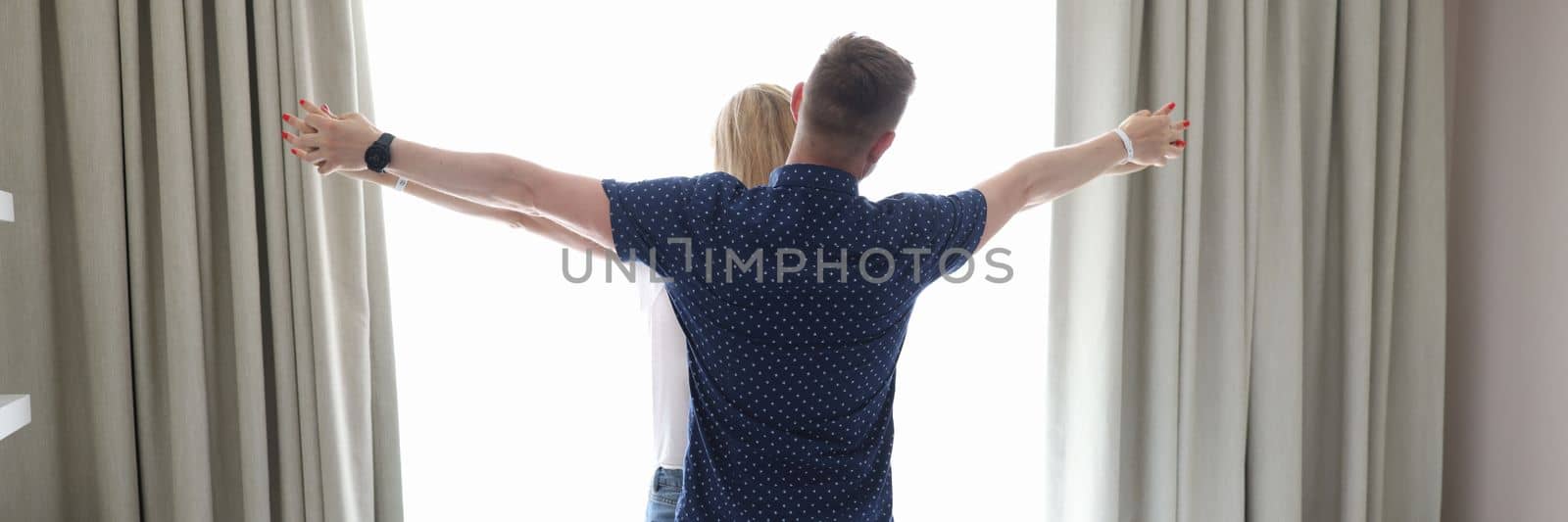 Married couple hugging and holding hands at window of hotel room in bedroom. Love romantic travel and honeymoon