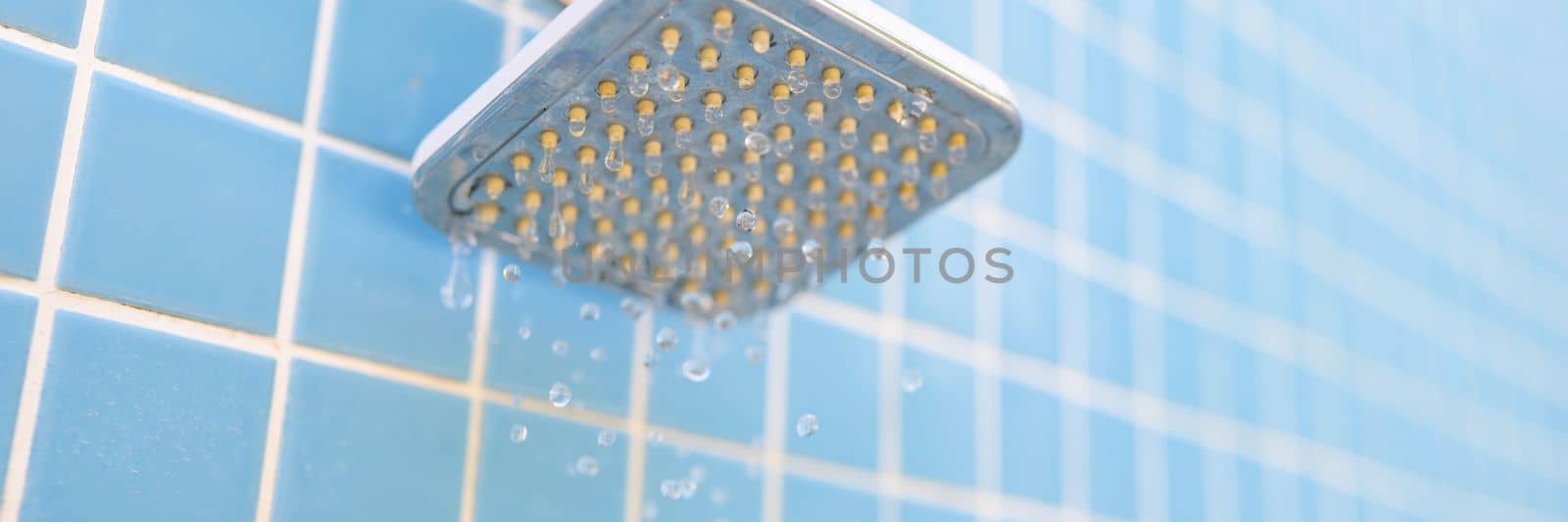 Wall-mounted outdoor shower and water drops on blue tile background. Summer showers for tourists in hotels