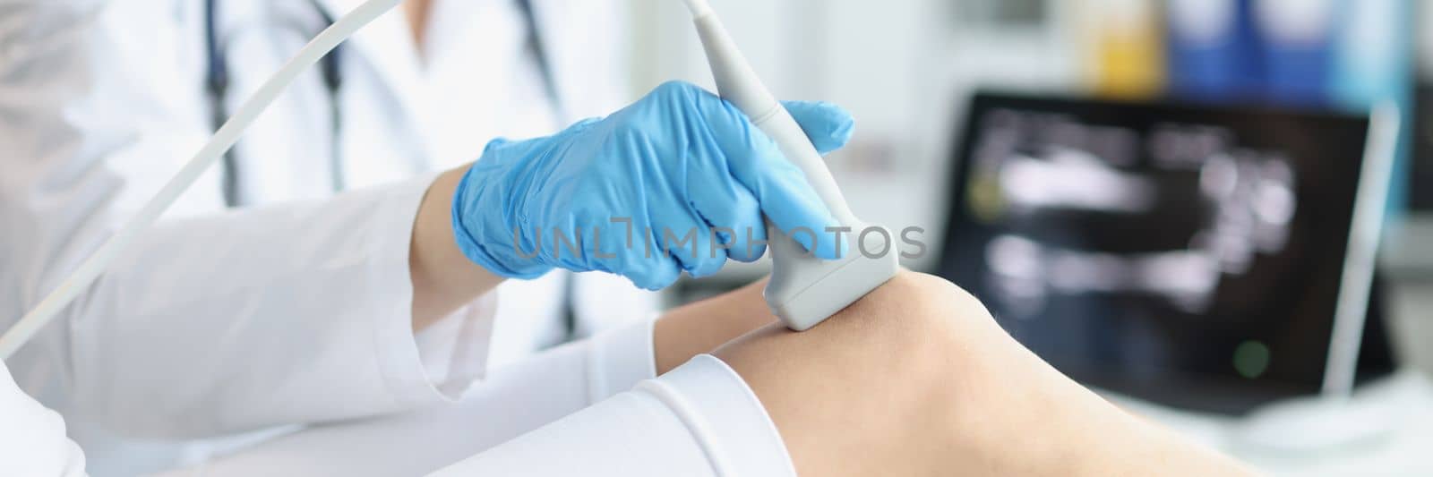 Orthopedic doctor makes ultrasound examination of patient knee in office. Young woman undergoing ultrasound of bones and joints of legs in clinic