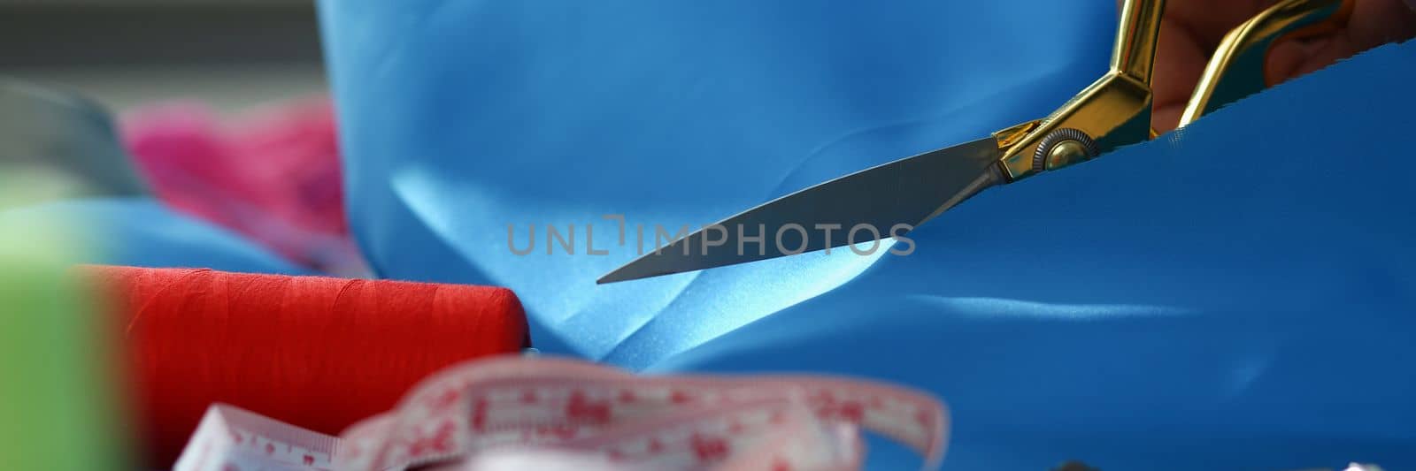 Woman hands cut blue fabric with tailor scissors closeup by kuprevich