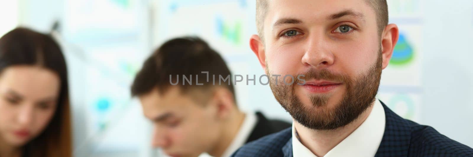 Portrait of smiling businessman with colleagues in a meeting in background in office. Business briefing and marketing training