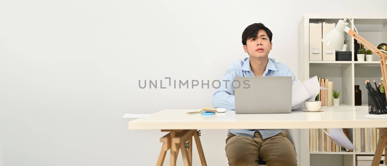 Young handsome businessman sitting at working desk and looking up at copy space. Horizontal banner, copy space for text.