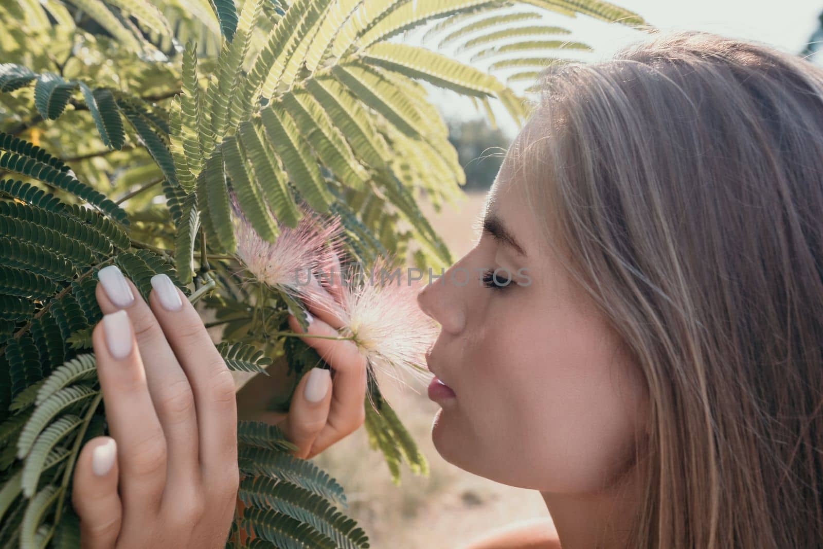 Beauty portrait of young woman closeup. Young girl smelling Chinese acacia pink blossoming flowers. Portrait of young woman in blooming spring, summer garden. Romantic vibe. Female and nature.