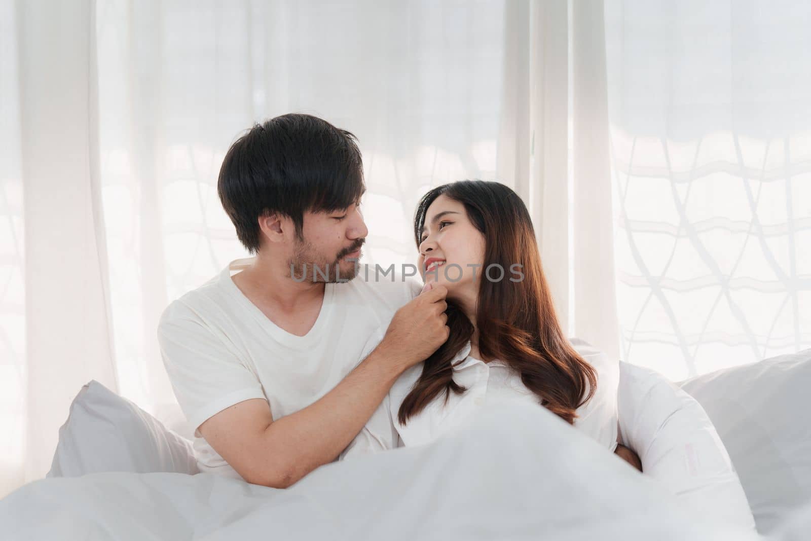 Beautiful asian couple in love and smiling sitting on bed. Romantic moment, relationships, family concept. by itchaznong