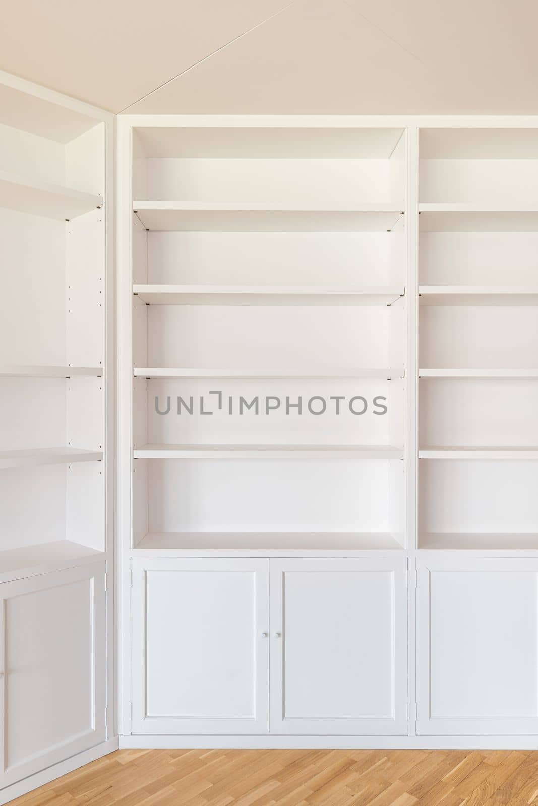 White wardrobes from floor to ceiling along the walls in the room. Many shelves for various interior items, books. From below lockers with doors for clothes, bed linen. The floor is wooden parquet
