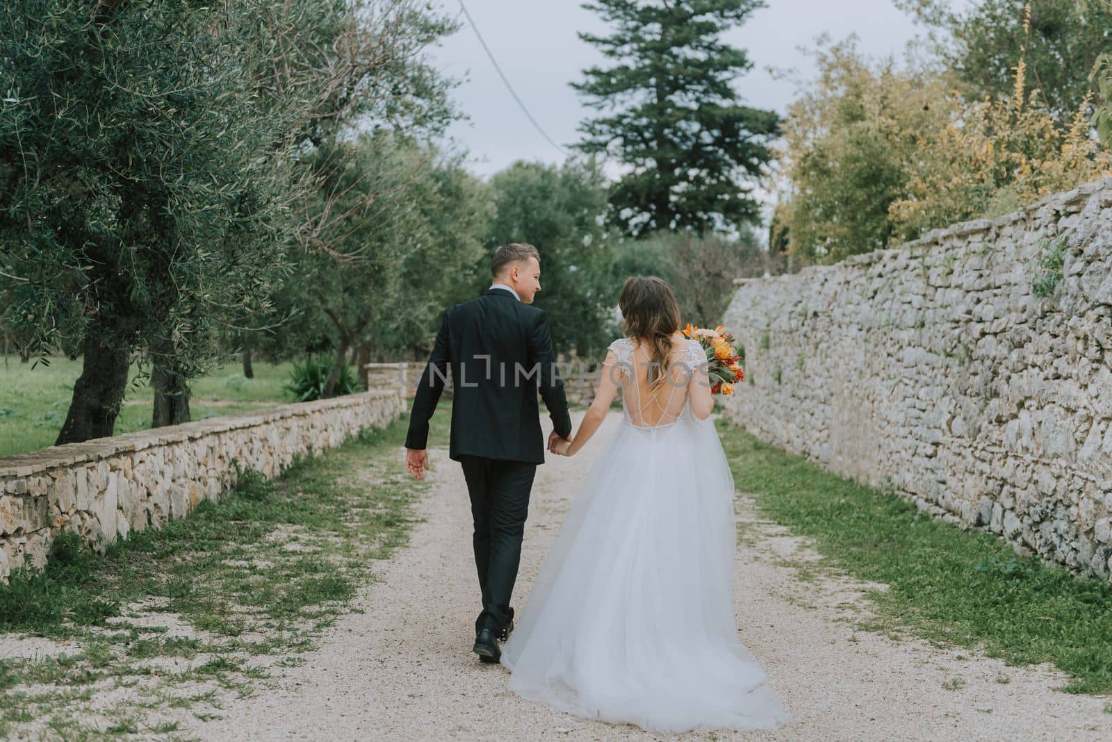 Happy stylish smiling couple walking in Tuscany, Italy on their wedding day. The bride and groom walk down the street by the hands. A stylish young couple walks. Husband and wife communicate nicely. Lovers run through the streets of the city by Andrii_Ko