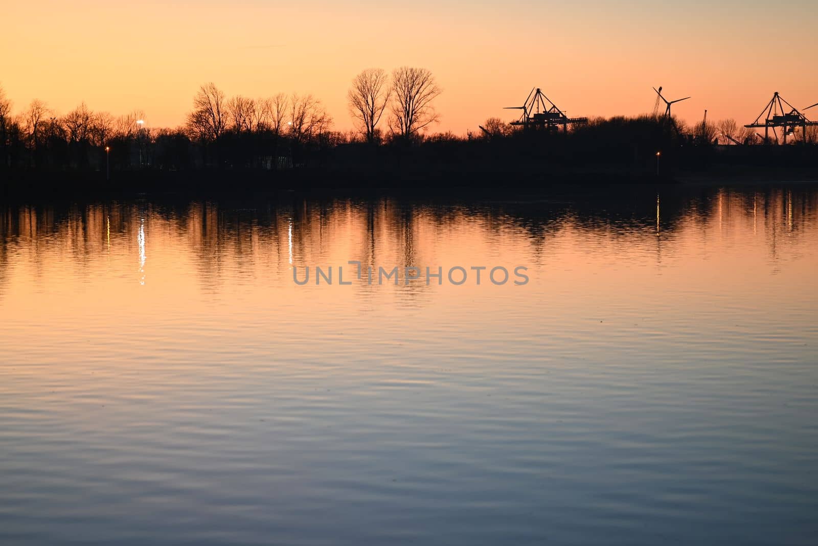 Evening mood besides a river against a container port and a beautyful sunset