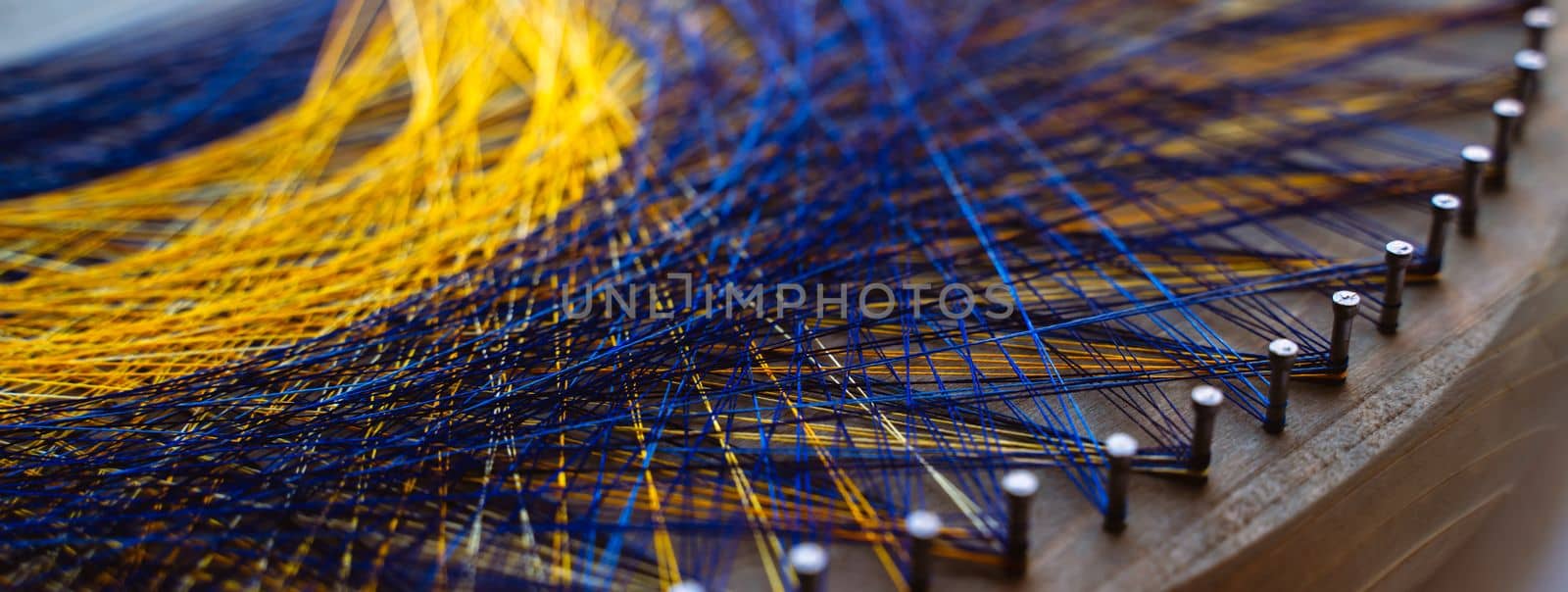 Colored thread mandala on a wooden board with nails. Mandala Moon Harmony Sun esotericism and psychology pictures from yellow and blue silk threads