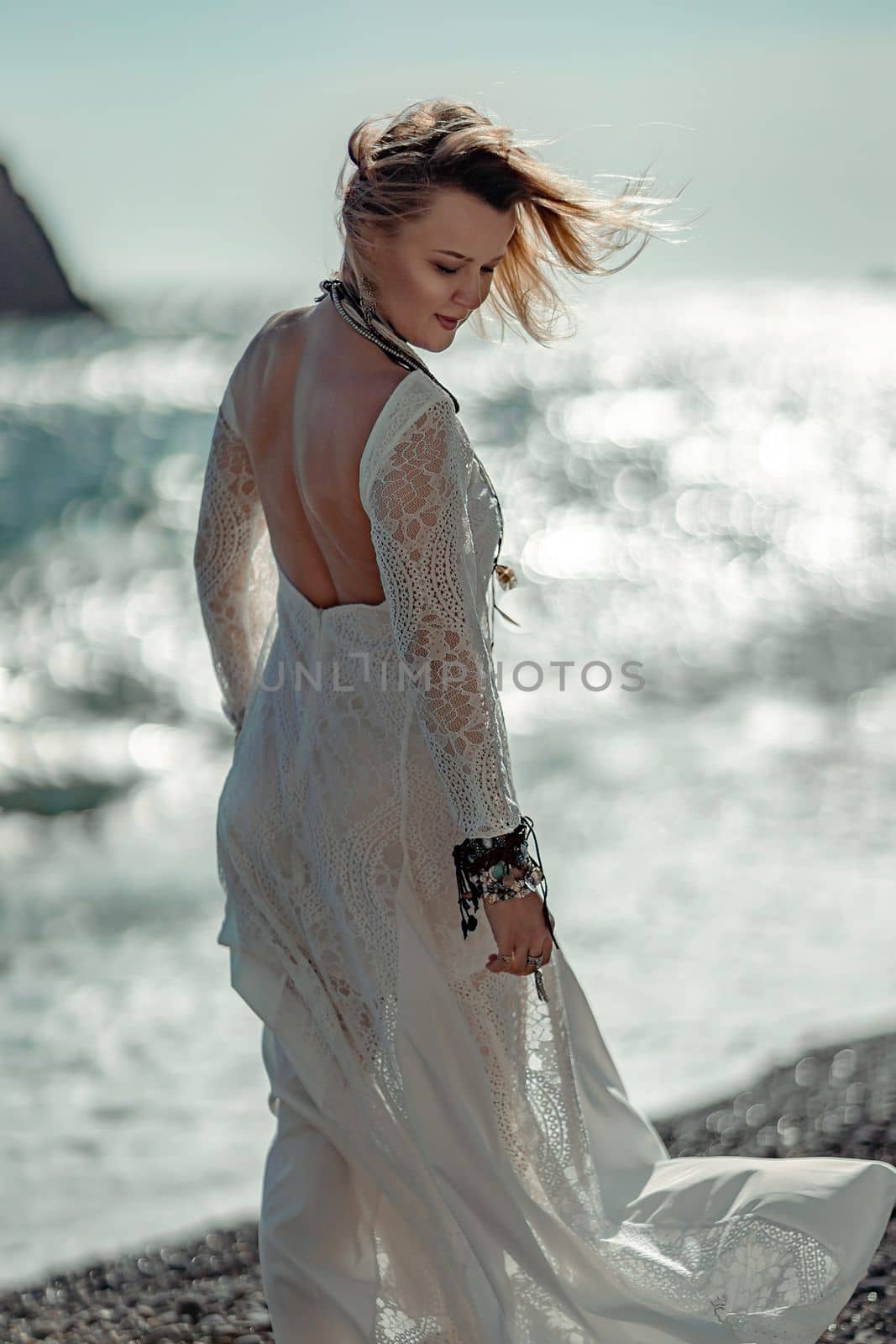 Woman beach sea white dress. The middle-aged looks good with blonde hair, boho style in a white long dress with beach decorations on the neck and arms