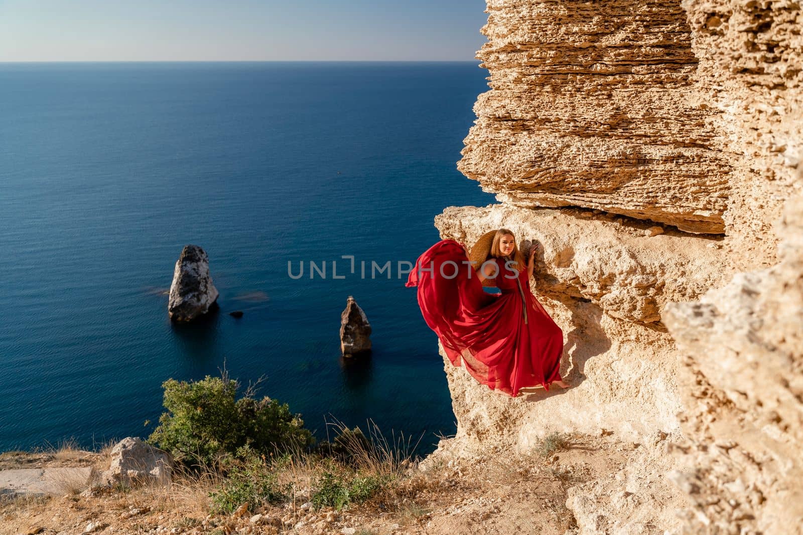 A woman in a red flying dress fluttering in the wind, against the backdrop of the sea