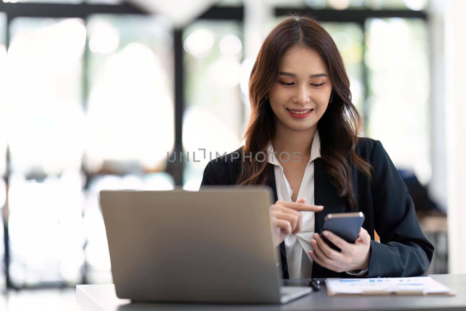 Asian businesswoman in formal suit in office happy and cheerful during using smartphone and working by nateemee