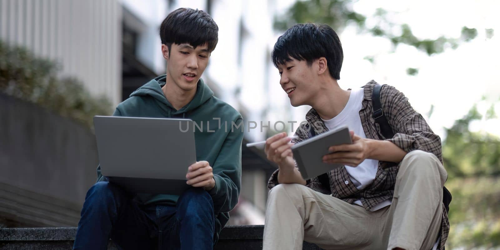 Two young Asian male college students discussing and working on their school project together by nateemee