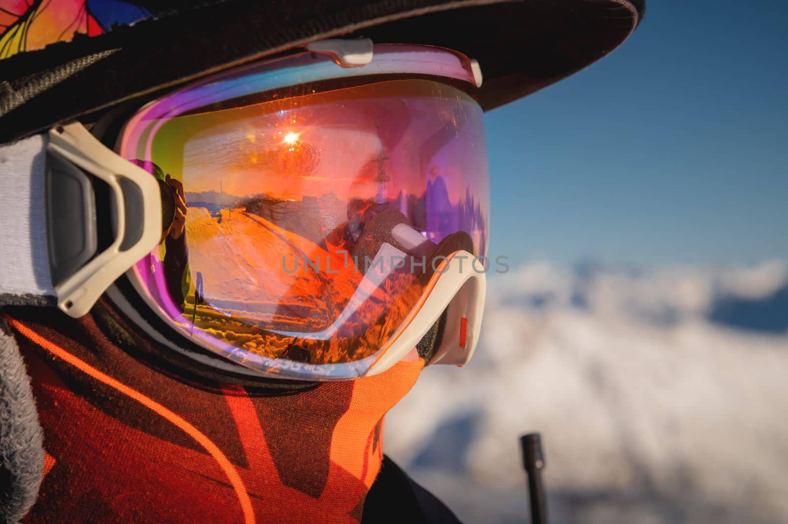 Ski goggles with reflection of snow-capped mountains. A man on a ski slope stands in profile and looks into the distance, portrait.