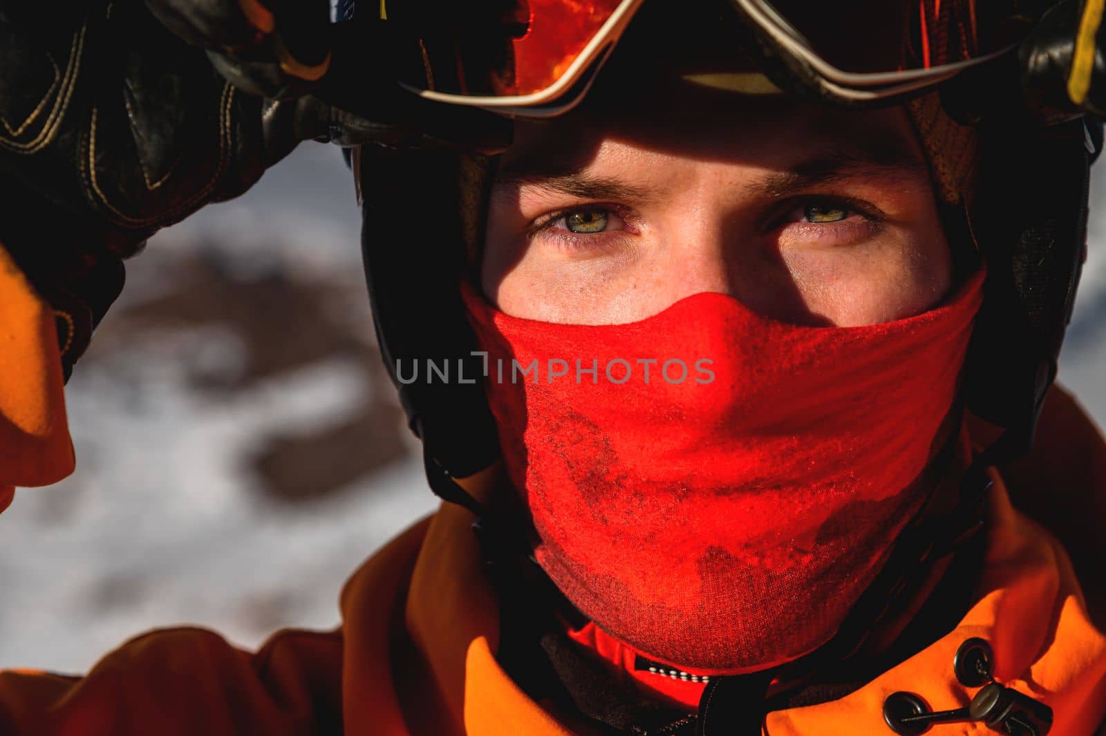 A young man looks directly into the camera, close-up of the eyes. Hands holding ski mask or goggles, expressive look.