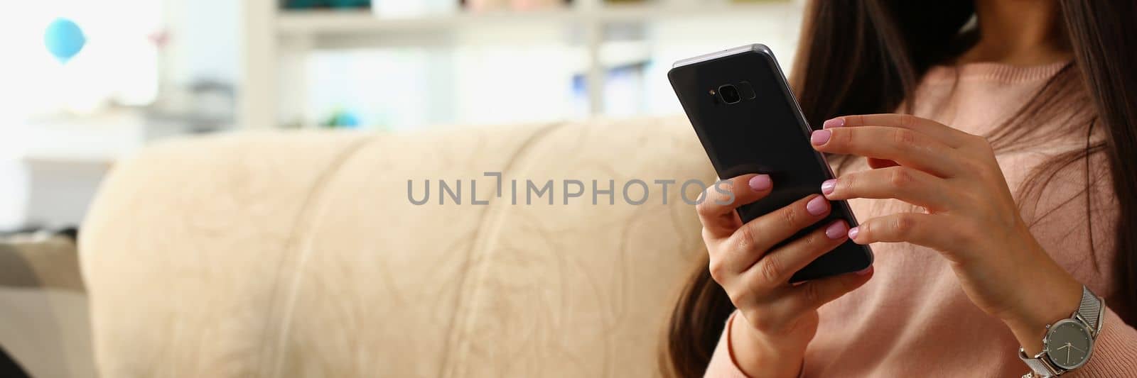 Woman using smartphone sitting on sofa at home by kuprevich