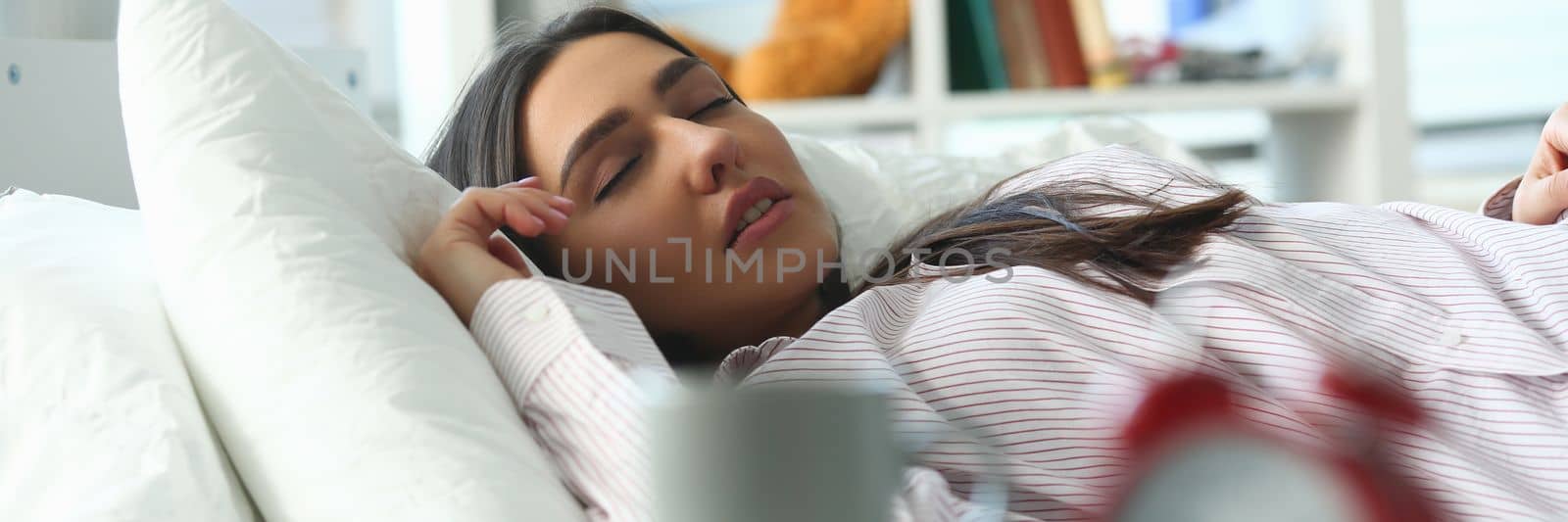Closeup of red alarm clock and calm peaceful young woman sleeping on bed in background. Morning serene dream concept