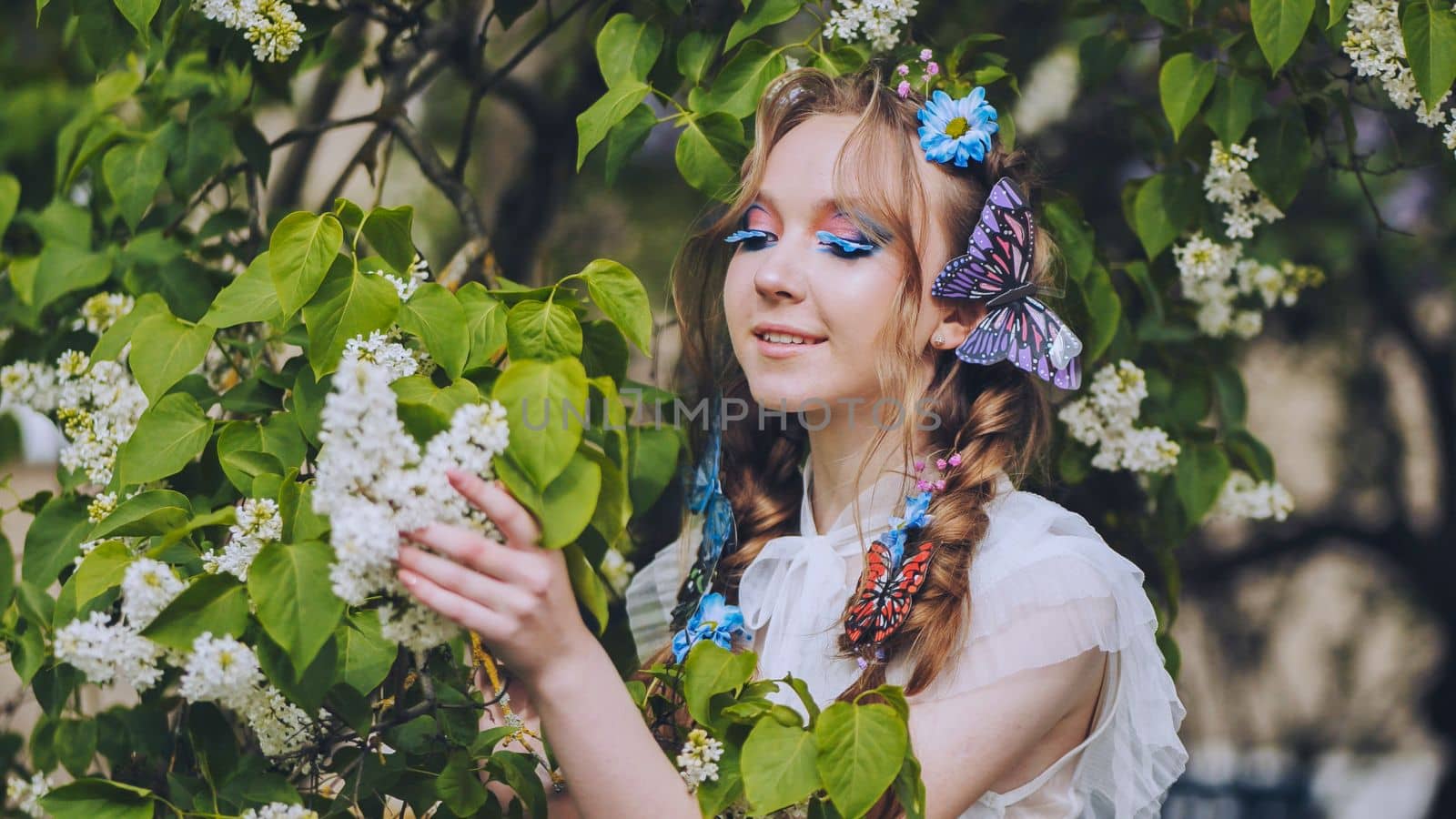 A young girl poses in white lilac with a beautiful hairstyle of flowers and butterflies
