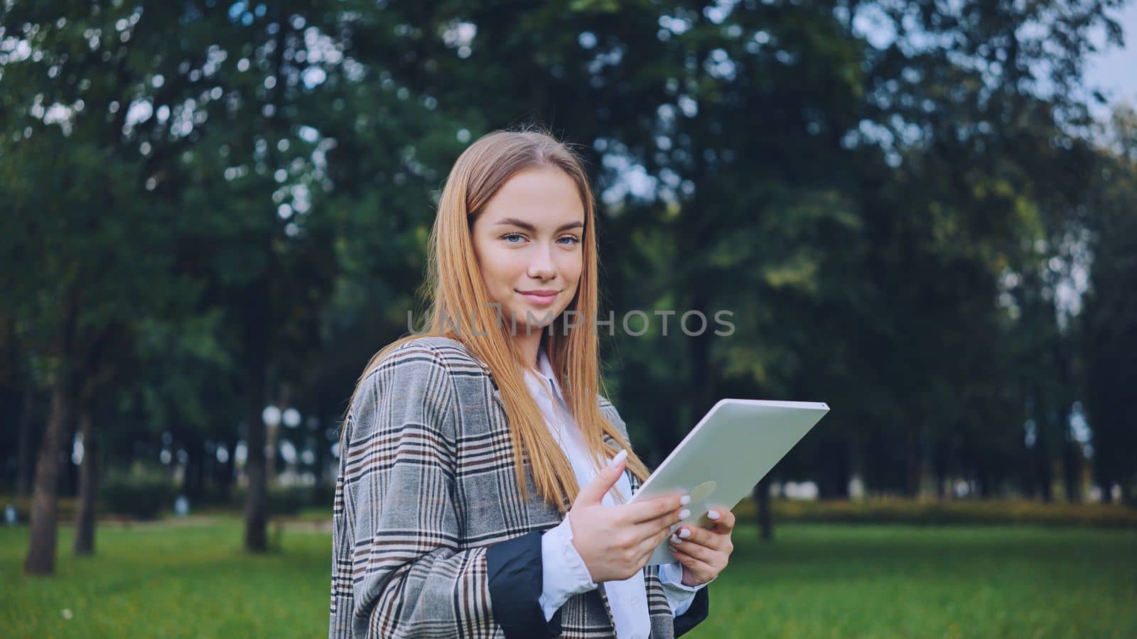 A young girl walks with a tablet in the park