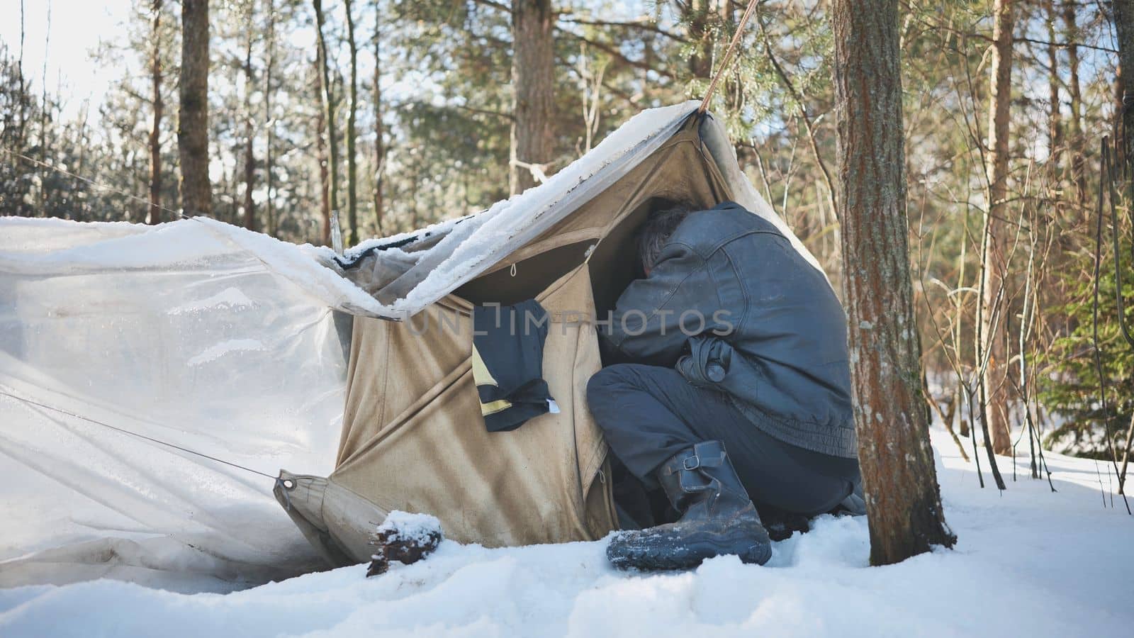 A homeless man climbs in and out of a tent in the woods in winter. by DovidPro