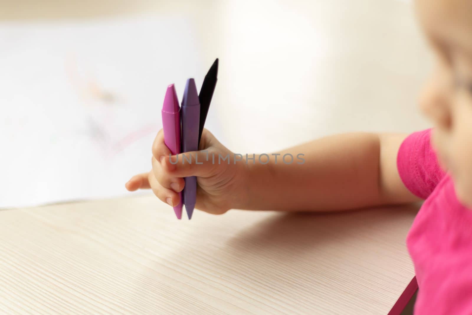 Little baby girl holding colorful wax crayons in hand. Concept of baby early development. Selective focus on hand. by Ri6ka