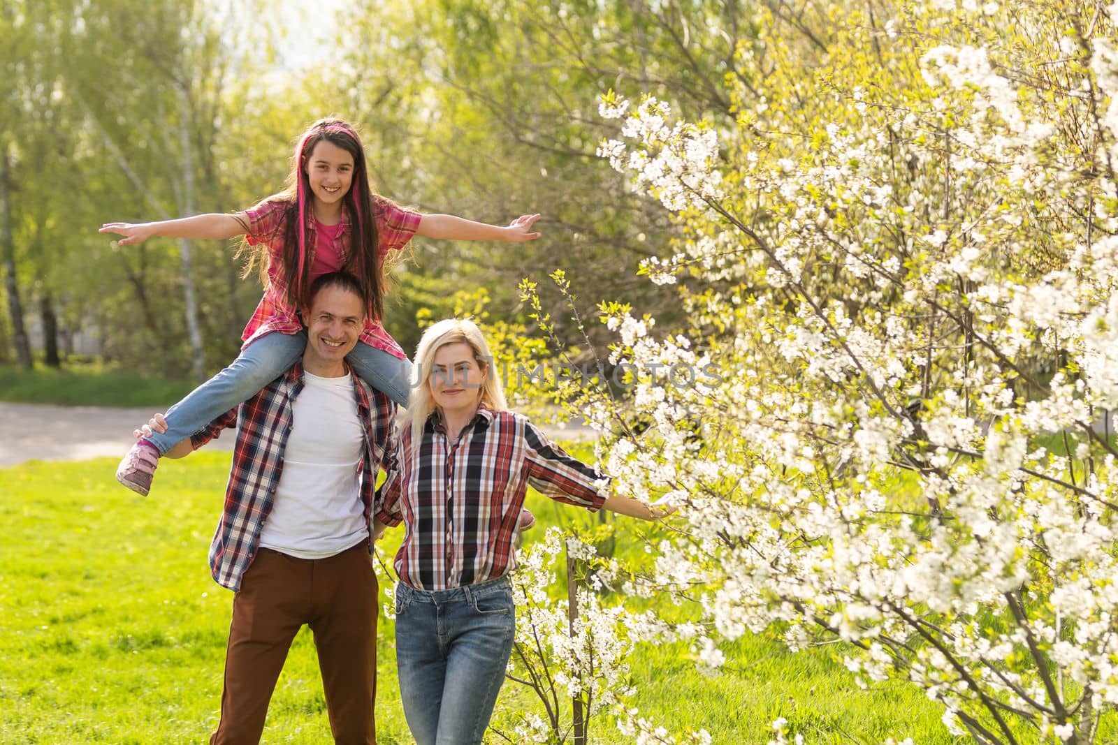 Happy parents mom and dad, daughter, young family outdoors in spring against the background of blooming apple and cherry trees by Andelov13