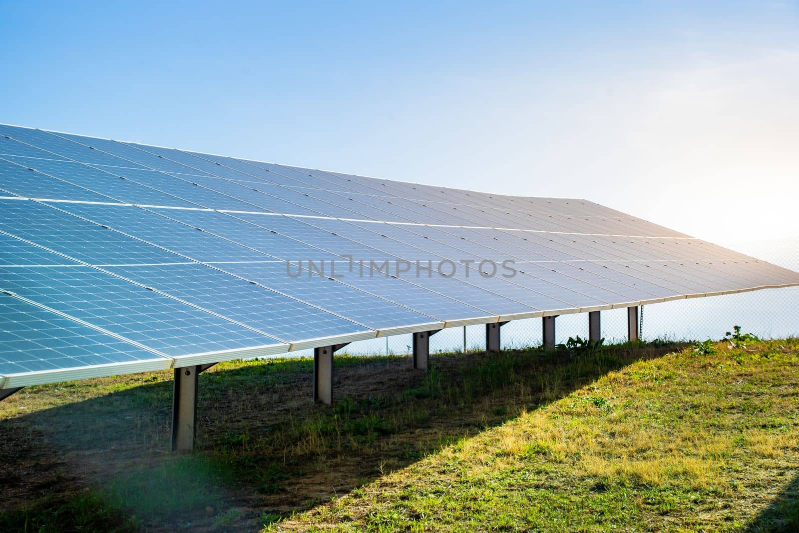Solar panels system in a green field with blue sky and the sun. Renewable and sustainable alternative energy production power generators from sun. Eco technology for better future.