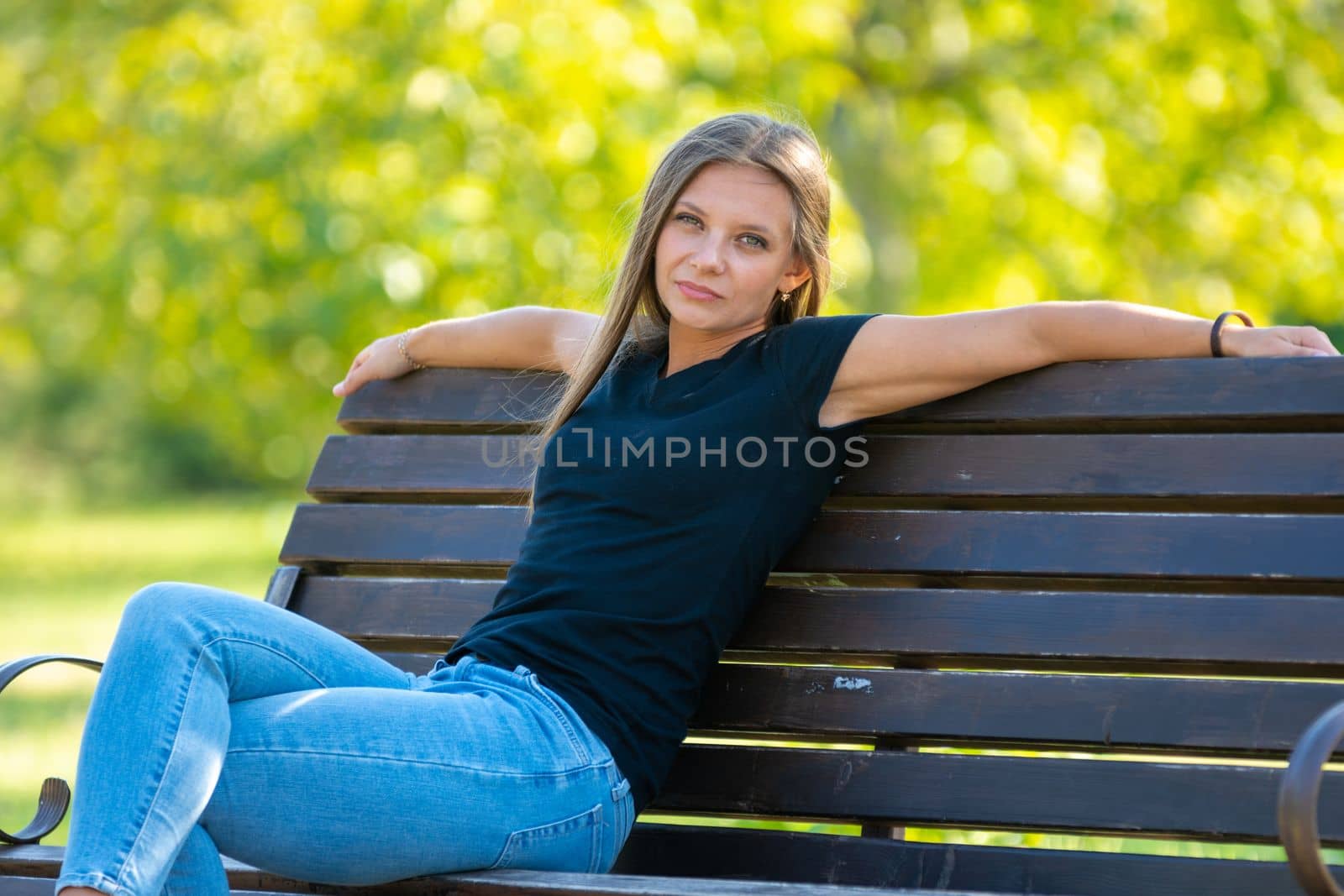 A girl sits on a bench in a sunny park and looks into the frame by Madhourse