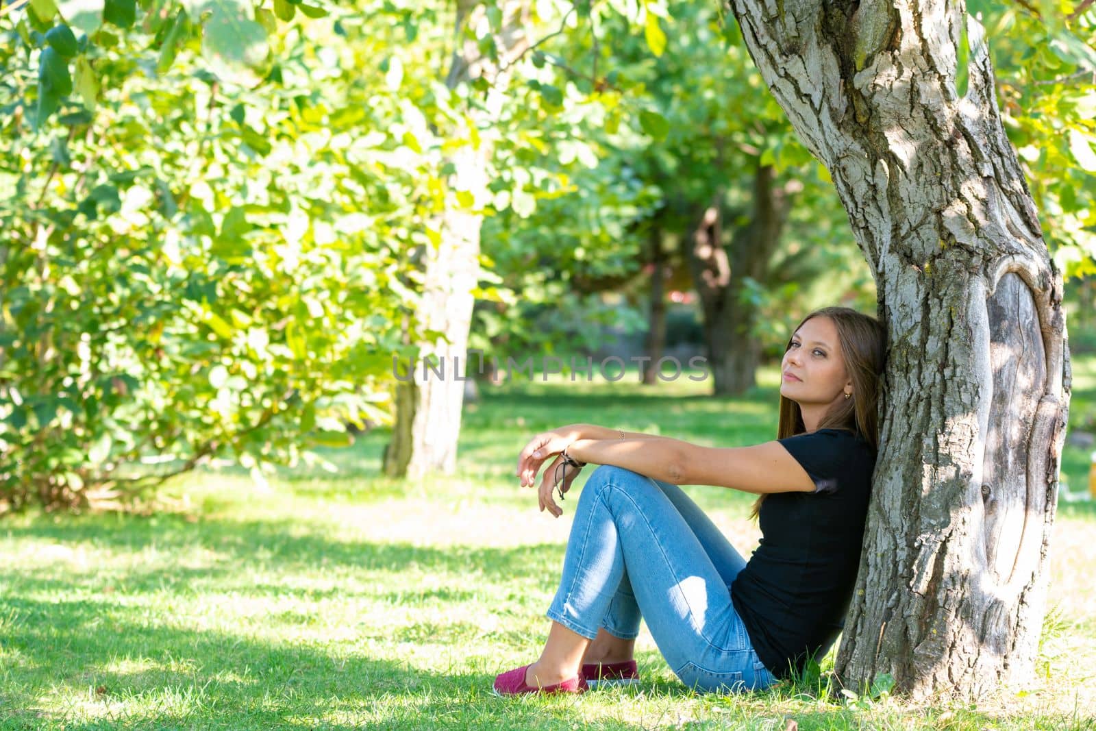 Girl sitting under a tree in a sunny park a