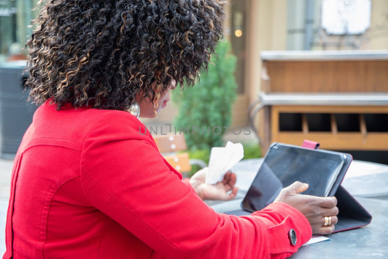 a young african american woman in a red coat sits at a table in a cafe and checking bill after shopping using a tablet, financial problems crisis, proper planning of expenses, High quality photo